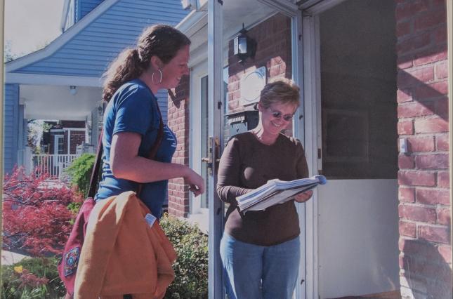Canvasser at doorstep speaking to a new Clean Water member signing a clipboard. 